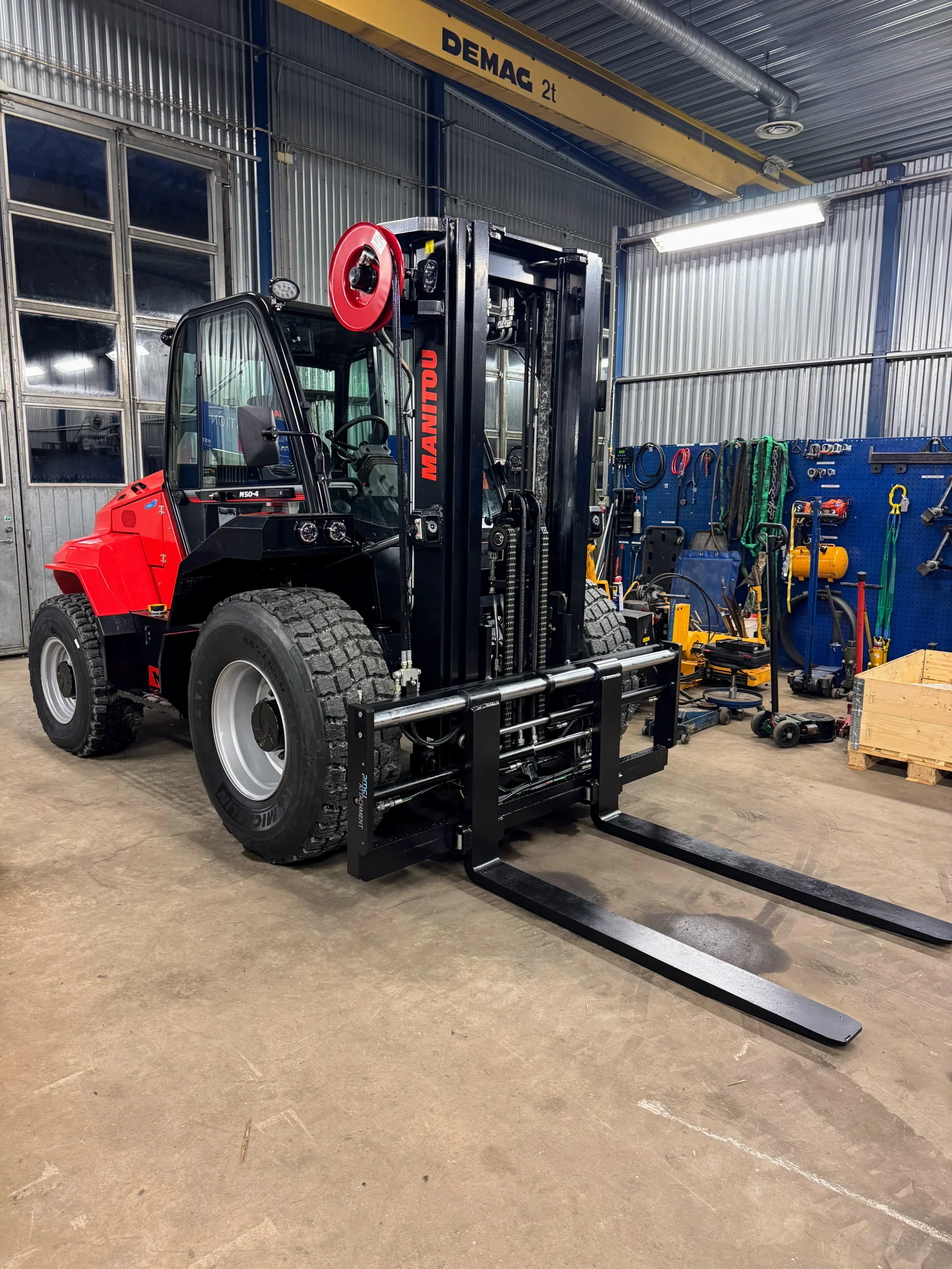 En röd Manitou M50-4 ST5 truck står parkerad inne i en industriverkstad, omgiven av olika verktyg och utrustning, redo för leverans eller kundanpassning för att passa dina specifika behov.