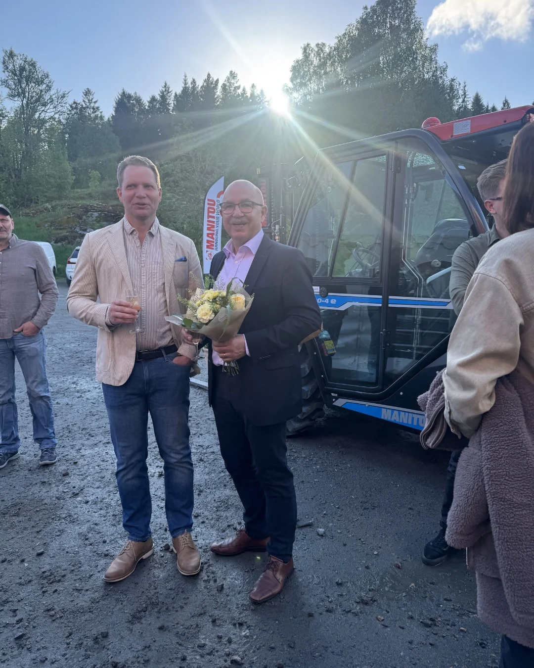 Två män poserar med blommor och kameran i fint väder.