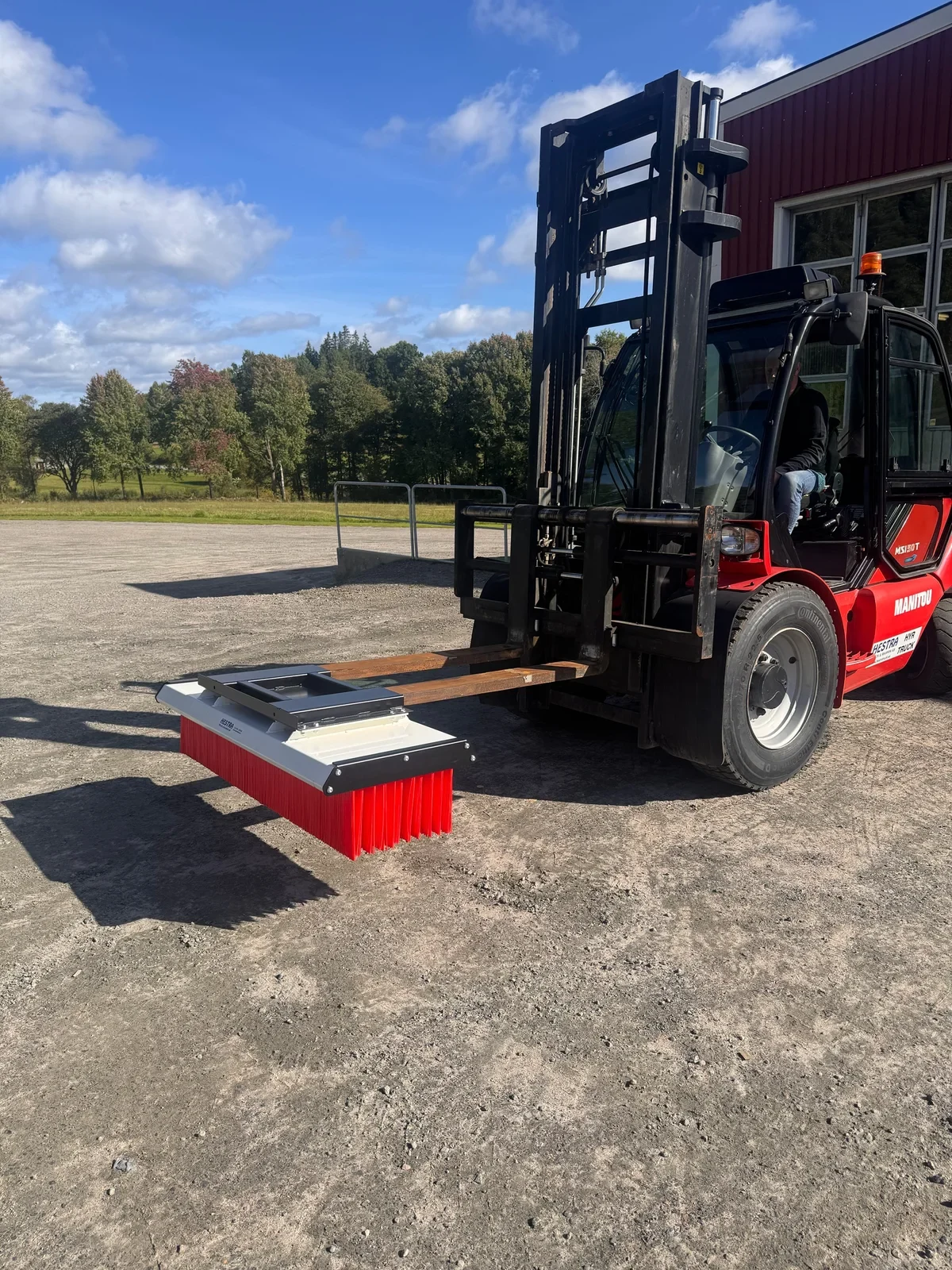 Sopborste med röd borst monterad framtill på gafflarna på en Manitou-truck